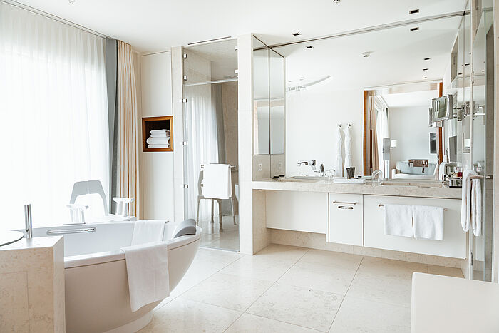 Elegantes, modernes Badezimmer mit doppeltem Waschtisch, großem Spiegel und einer Dusche mit Glasabtrennung. Sanfte Beleuchtung und neutrale Töne schaffen eine ruhige Atmosphäre.